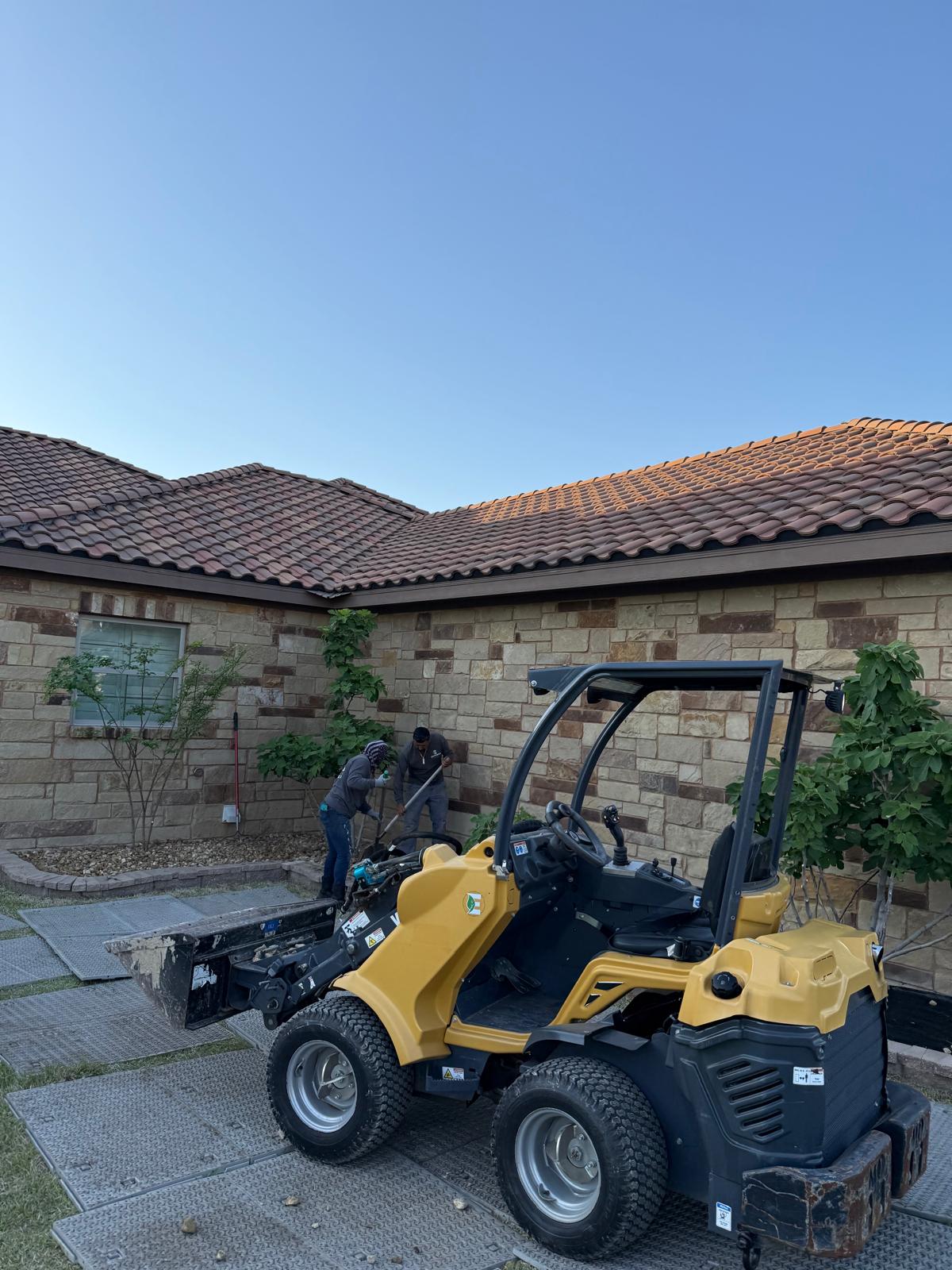 Estrada Treescapes crew clearing landscaping beds with a compact loader beside a Central Texas home